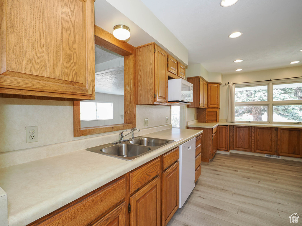 Kitchen with light hardwood / wood-style floors, white appliances, and sink