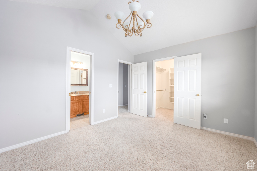 Unfurnished bedroom featuring a closet, a walk in closet, an inviting chandelier, connected bathroom, and light colored carpet