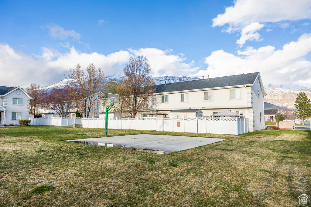 Rear view of house with a yard, a mountain view, and basketball court