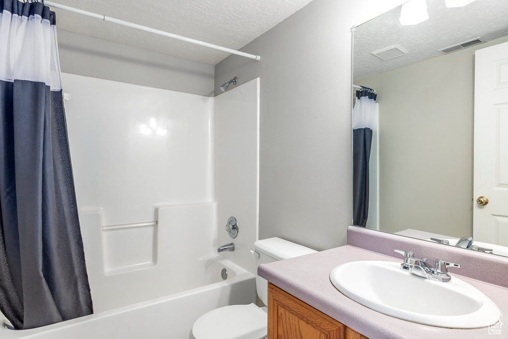 Full bathroom with shower / tub combo, vanity, a textured ceiling, and toilet