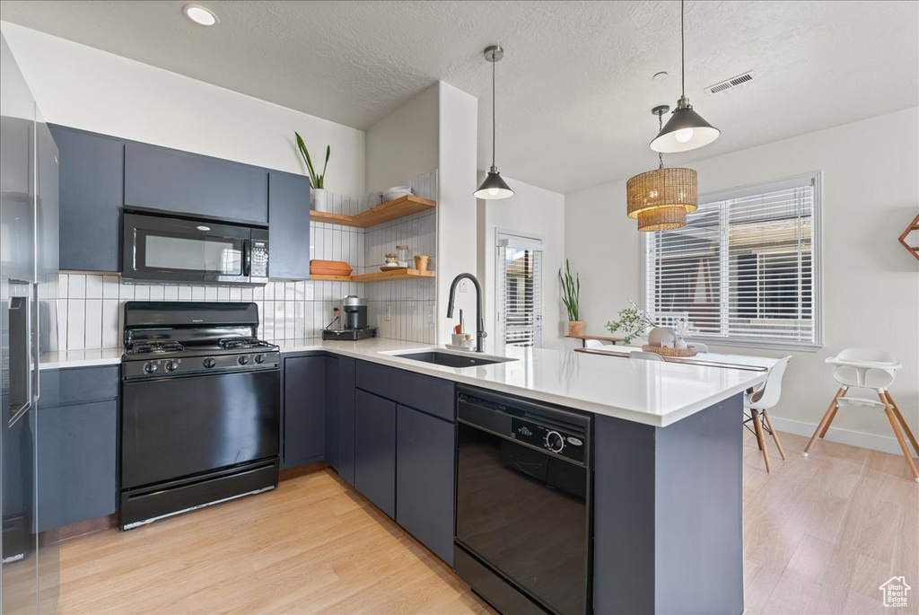 Kitchen with backsplash, light wood-type flooring, black appliances, and sink