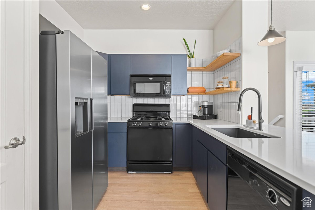 Kitchen with tasteful backsplash, decorative light fixtures, black appliances, and sink