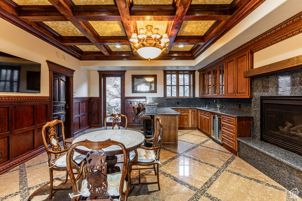 Kitchen featuring light tile floors, ornamental molding, coffered ceiling, wine cooler, and a notable chandelier