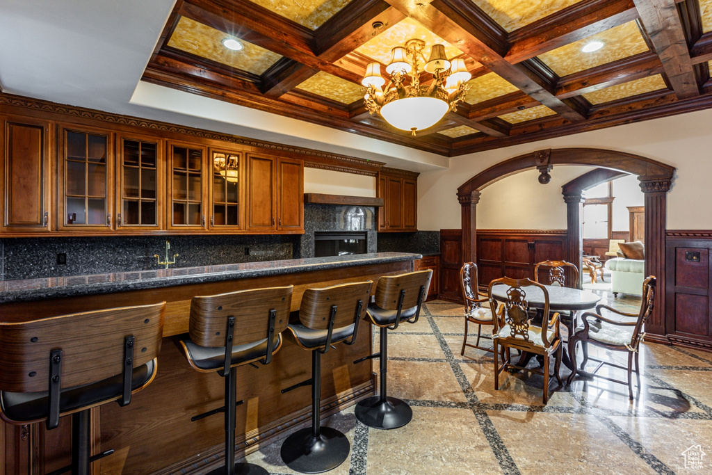 Interior space featuring light tile floors, backsplash, decorative columns, coffered ceiling, and an inviting chandelier