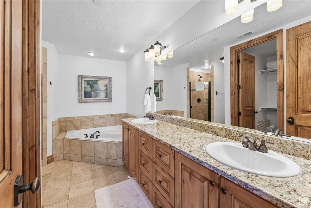 Bathroom with large vanity, a textured ceiling, separate shower and tub, dual sinks, and tile flooring