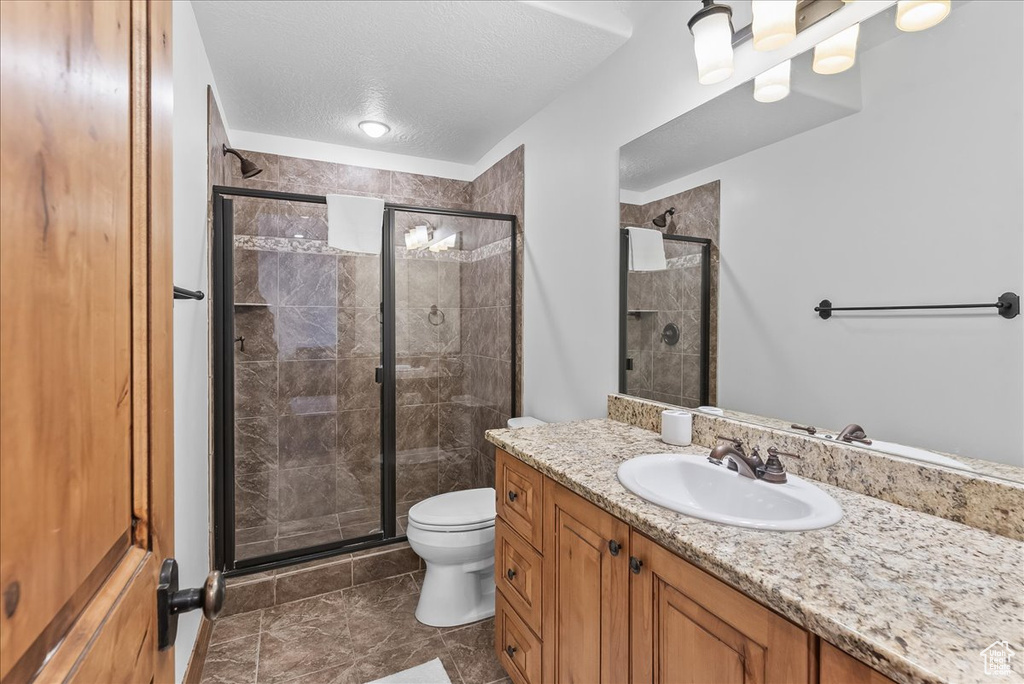 Bathroom featuring vanity, walk in shower, tile floors, a textured ceiling, and toilet