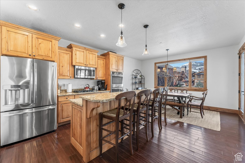 Kitchen featuring light stone countertops, decorative light fixtures, appliances with stainless steel finishes, a center island, and dark hardwood / wood-style flooring