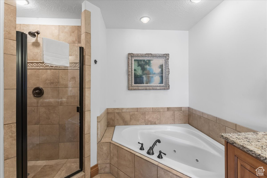 Bathroom featuring a textured ceiling, separate shower and tub, and vanity