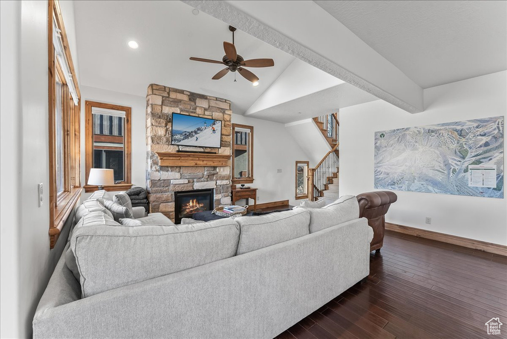 Living room with ceiling fan, a stone fireplace, dark wood-type flooring, and lofted ceiling with beams