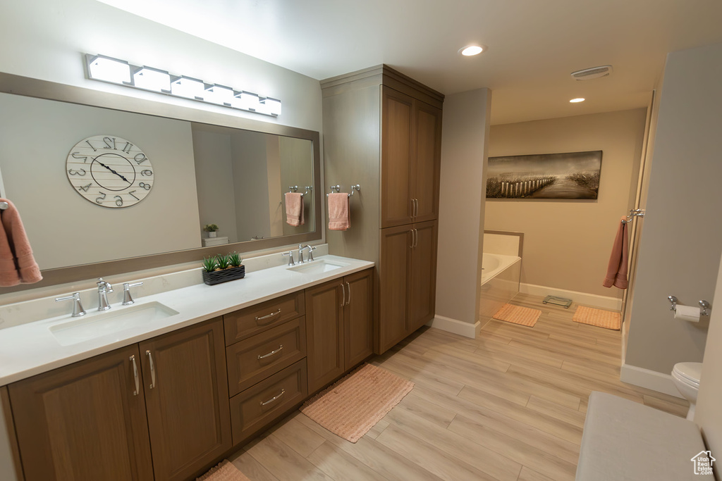 Bathroom featuring toilet, oversized vanity, double sink, a bathing tub, and hardwood / wood-style flooring