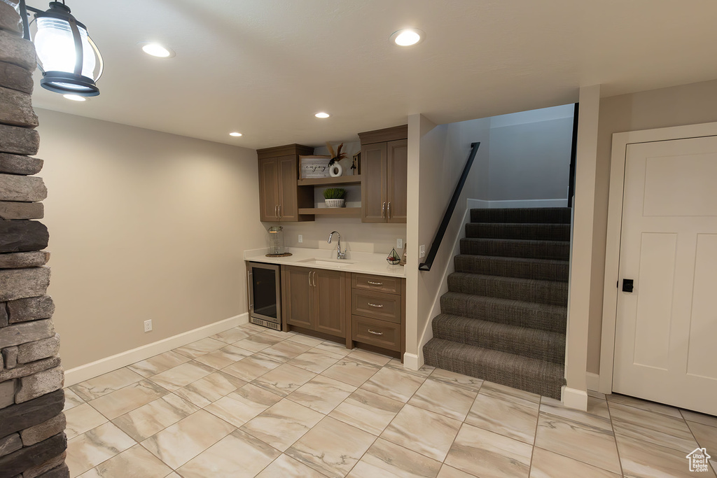 Kitchen with dark brown cabinetry, beverage cooler, light tile floors, and sink
