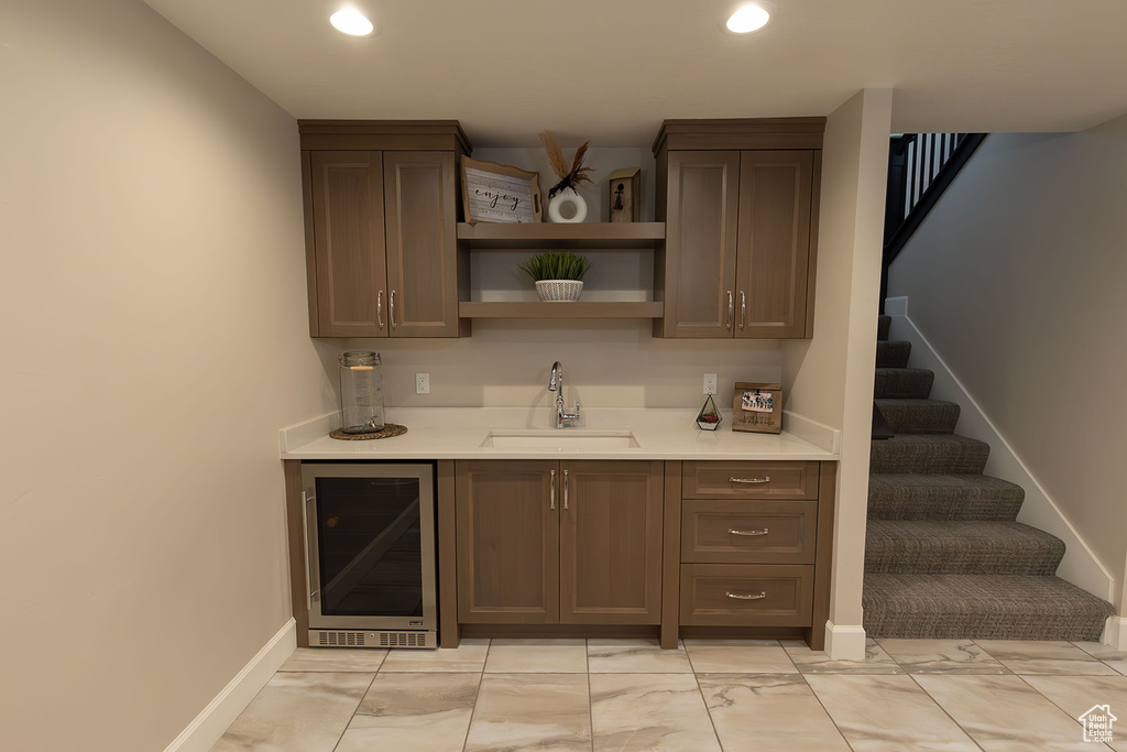 Bar featuring dark brown cabinetry, wine cooler, light tile floors, and sink