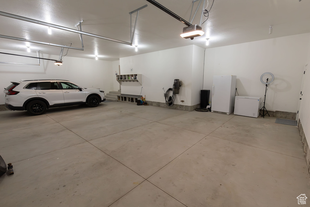 Garage with a garage door opener, refrigerator, and white fridge