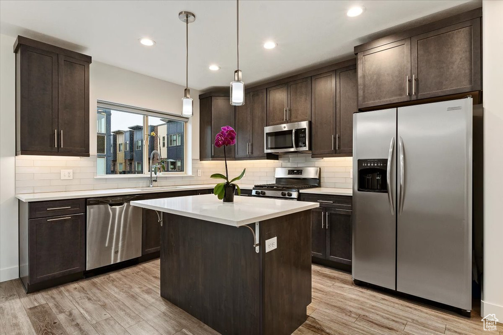 Kitchen with appliances with stainless steel finishes, light hardwood / wood-style flooring, tasteful backsplash, decorative light fixtures, and a center island