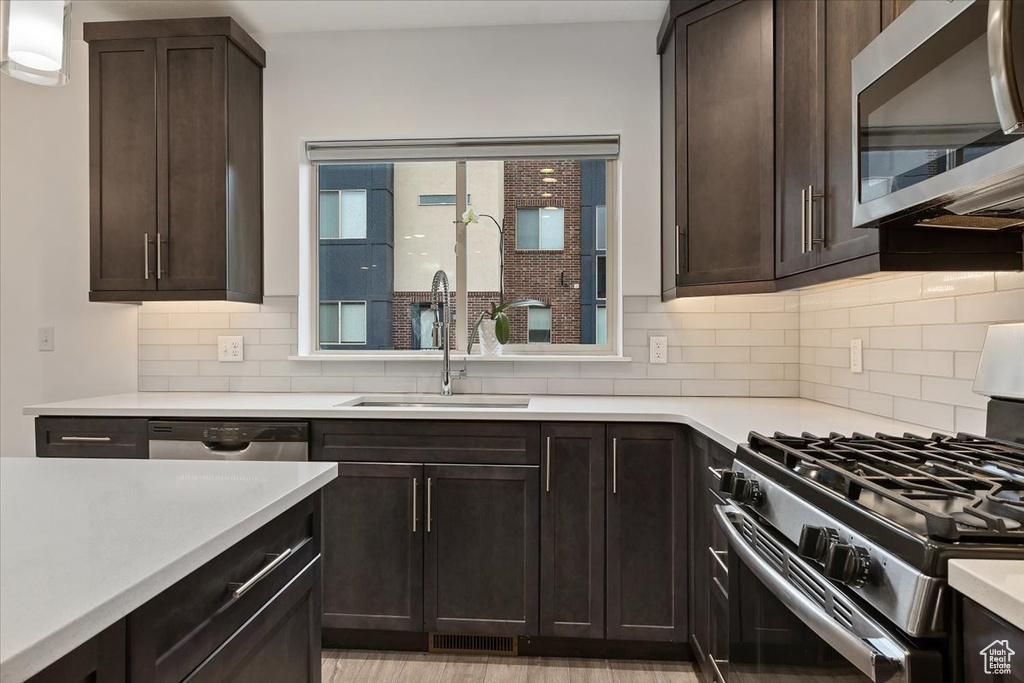 Kitchen with appliances with stainless steel finishes, sink, light wood-type flooring, tasteful backsplash, and dark brown cabinetry