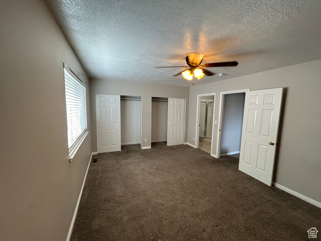Unfurnished bedroom featuring dark carpet, multiple closets, ceiling fan, and a textured ceiling