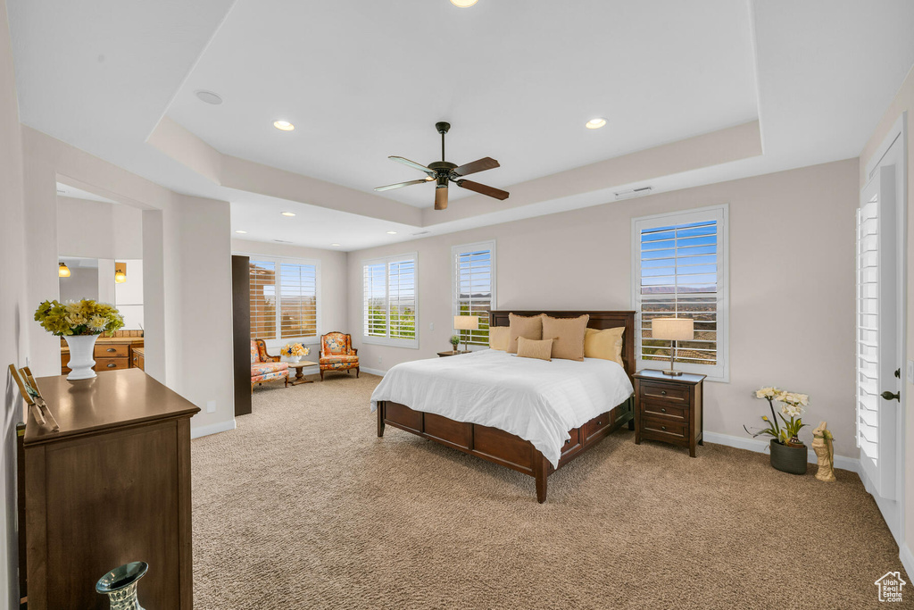 Bedroom featuring light carpet, a tray ceiling, and ceiling fan