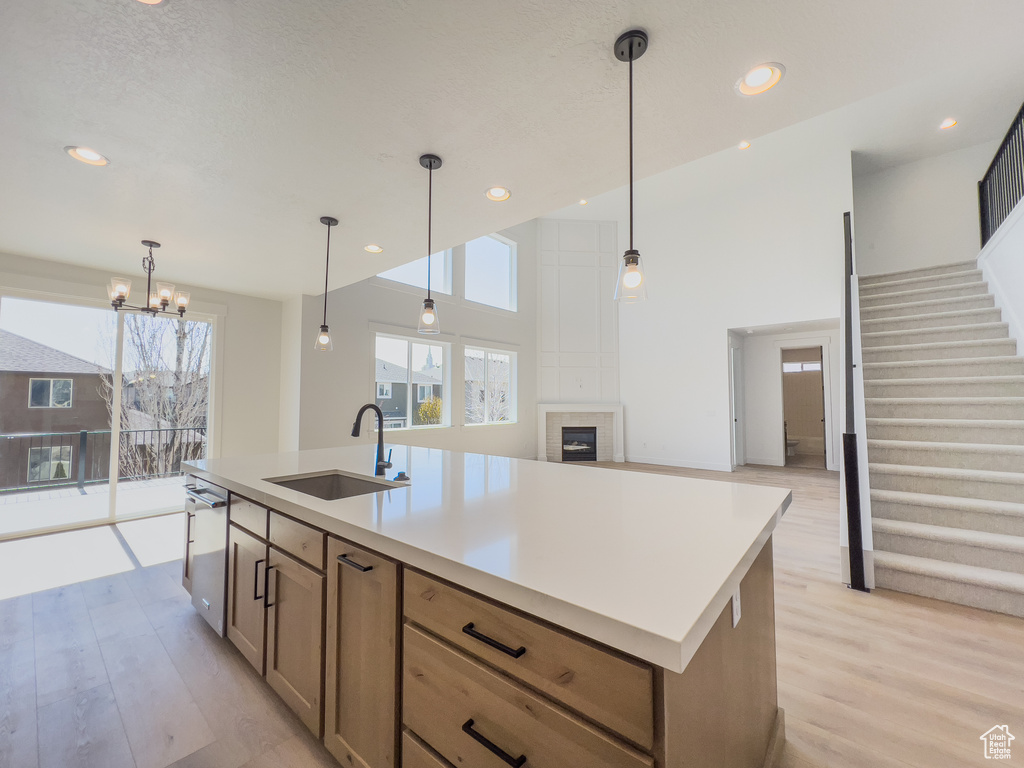 Kitchen featuring decorative light fixtures, light hardwood / wood-style floors, sink, a center island with sink, and stainless steel dishwasher
