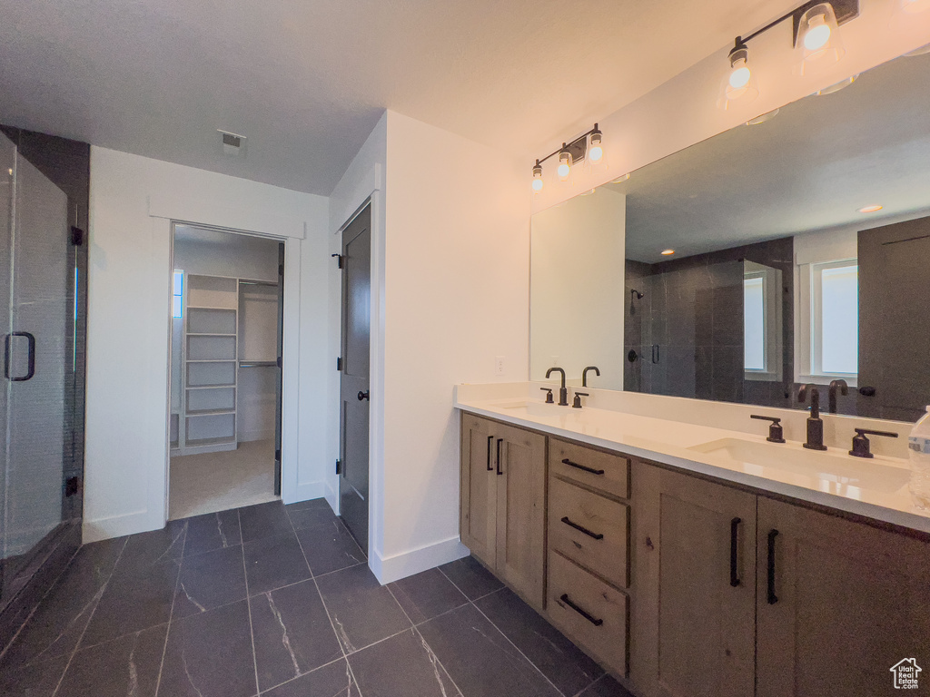 Bathroom featuring double sink, tile floors, a shower with shower door, and vanity with extensive cabinet space