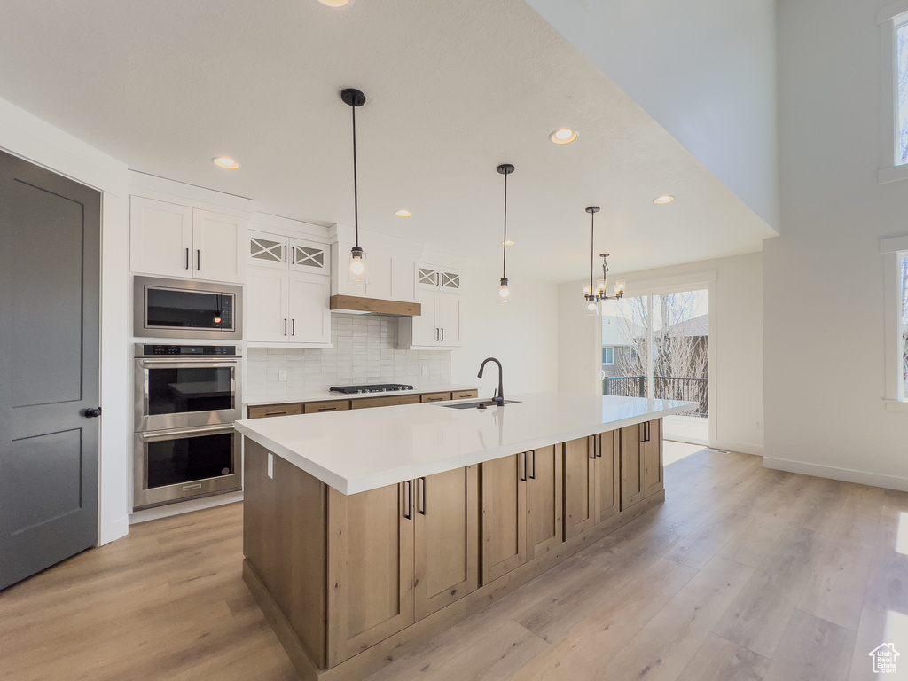 Kitchen featuring stainless steel appliances, tasteful backsplash, a center island with sink, white cabinets, and light wood-type flooring