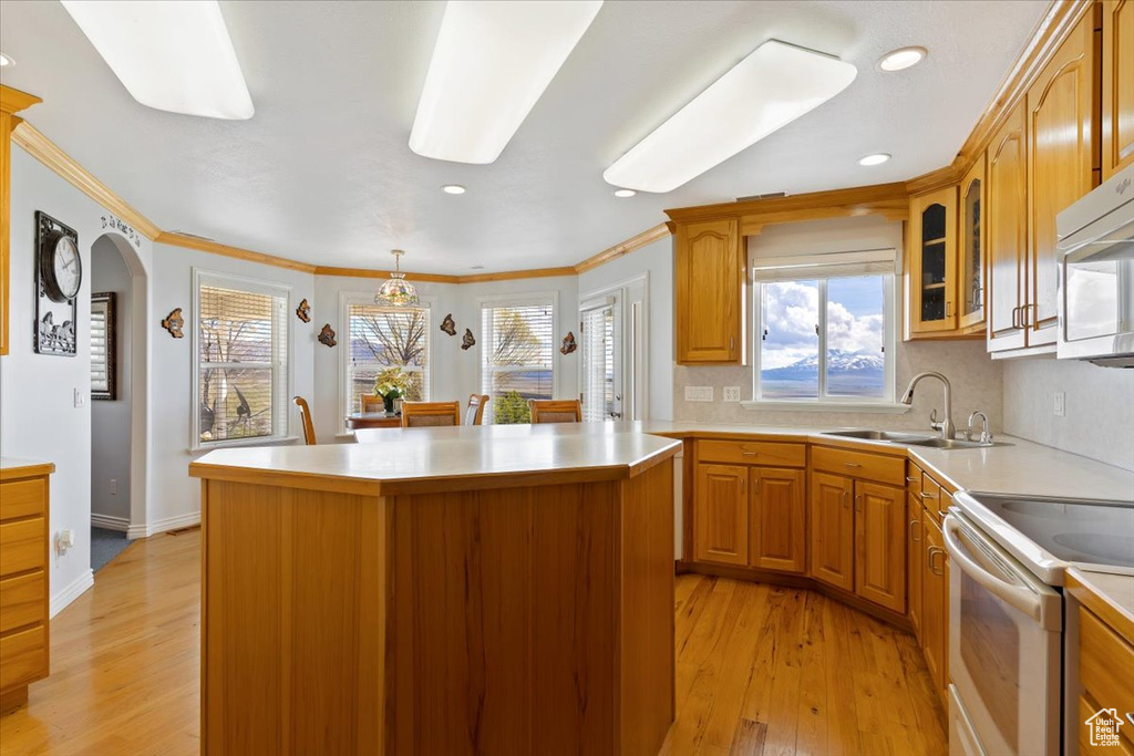 Kitchen with decorative light fixtures, white appliances, light hardwood / wood-style floors, sink, and a kitchen island