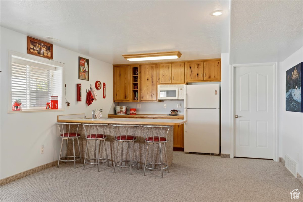 Kitchen with white appliances, light carpet, a kitchen breakfast bar, and kitchen peninsula
