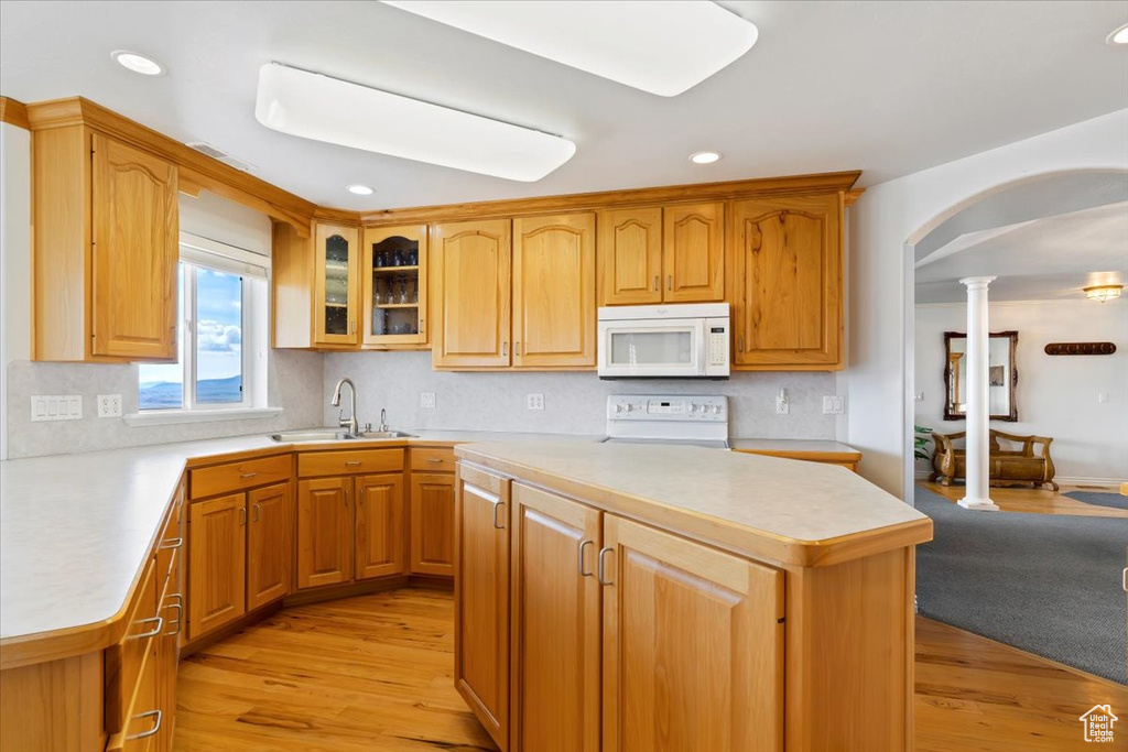 Kitchen featuring white appliances, ornate columns, sink, and light hardwood / wood-style flooring