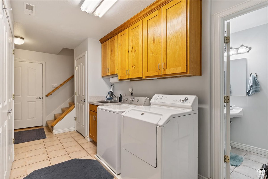 Clothes washing area with cabinets, light tile flooring, independent washer and dryer, and sink