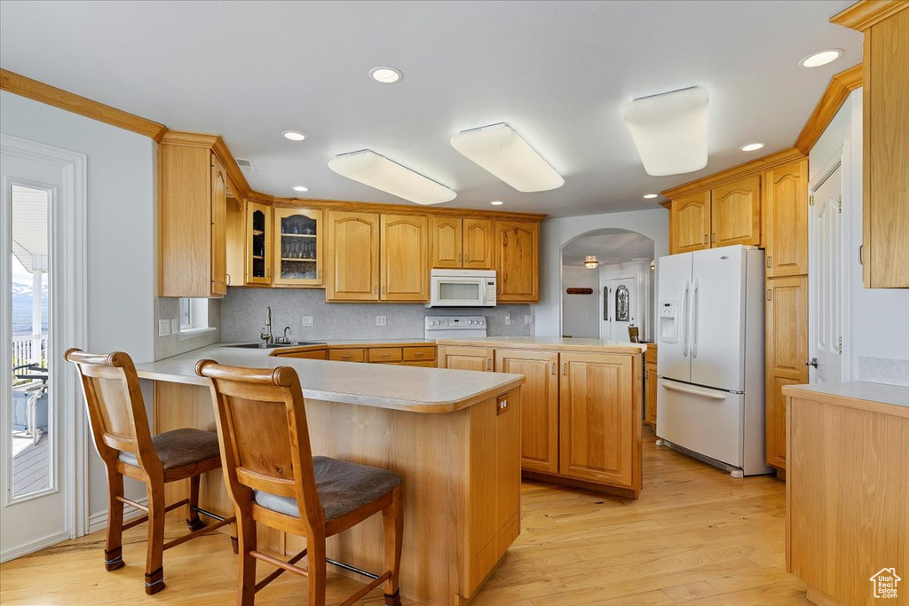 Kitchen with white appliances, a kitchen bar, sink, light hardwood / wood-style flooring, and tasteful backsplash