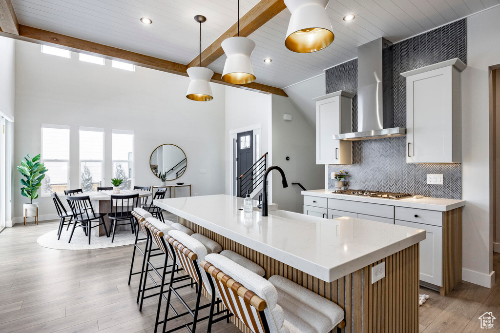 Kitchen featuring an island with sink, pendant lighting, white cabinets, a breakfast bar, and wall chimney exhaust hood