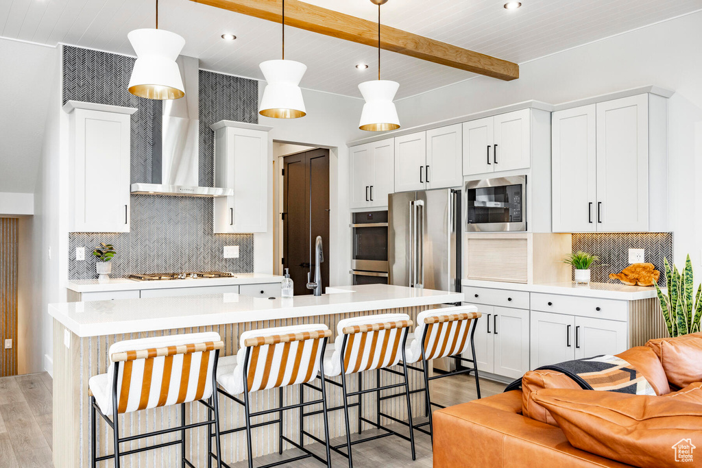 Kitchen featuring a breakfast bar, light hardwood / wood-style flooring, backsplash, stainless steel appliances, and decorative light fixtures