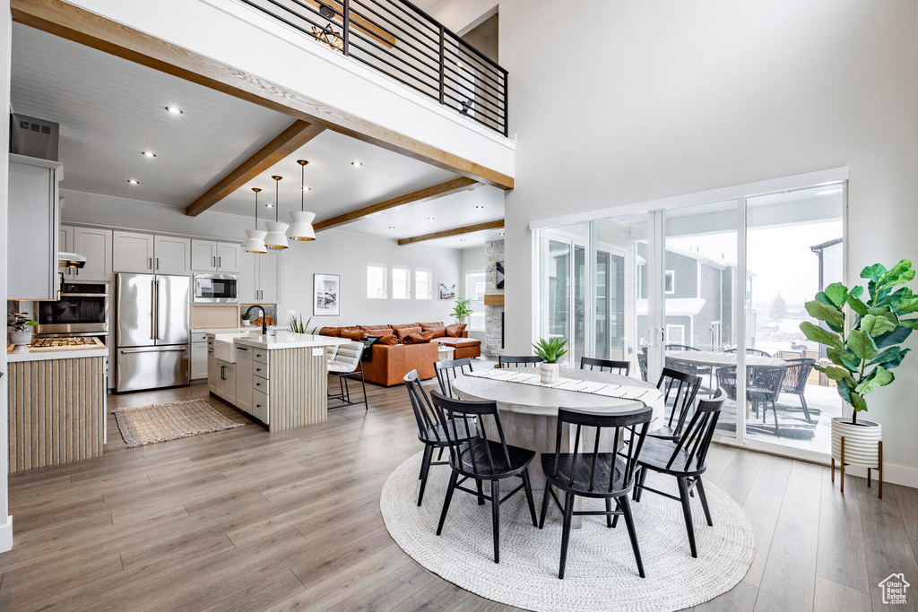Dining space featuring beam ceiling, a high ceiling, light hardwood / wood-style floors, and a wealth of natural light