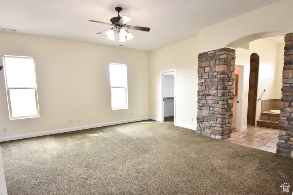 Empty room with light carpet, decorative columns, ceiling fan, and brick wall