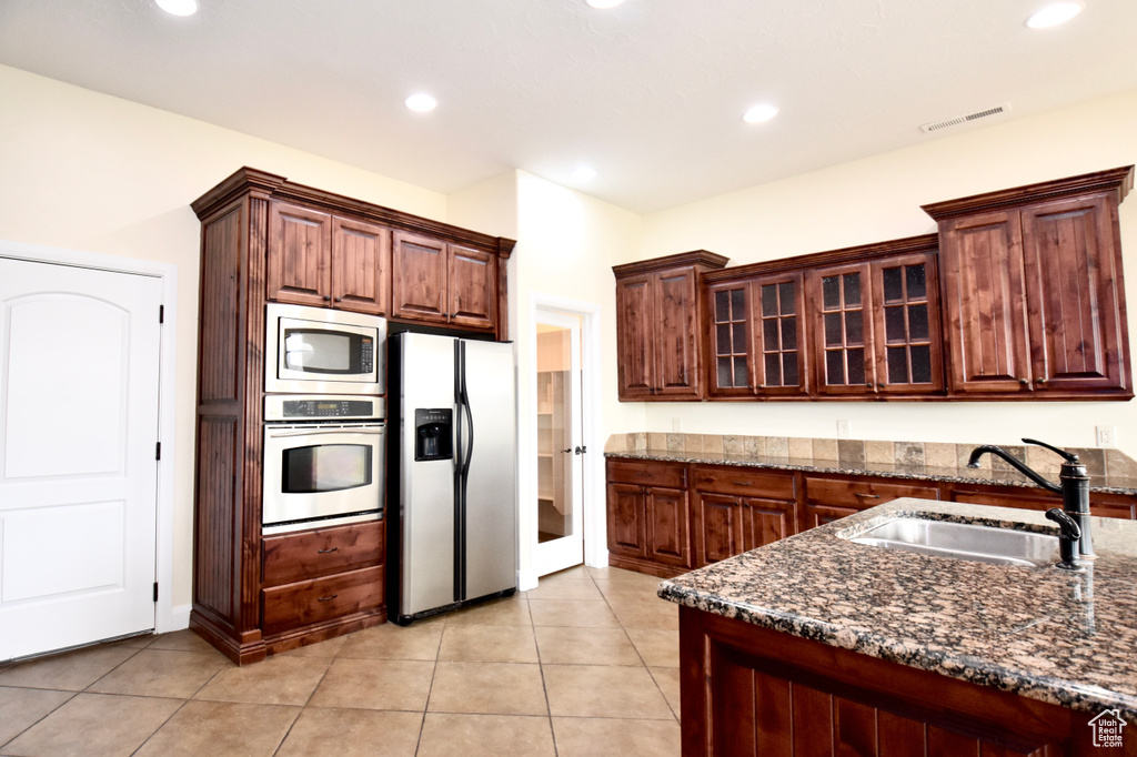 Kitchen featuring stainless steel appliances, sink, light tile floors, and dark stone countertops
