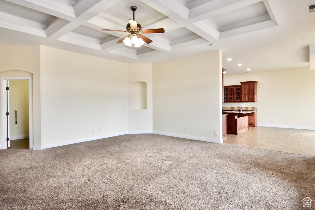 Unfurnished living room with coffered ceiling, ceiling fan, beamed ceiling, sink, and light colored carpet