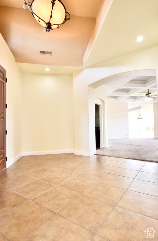 Empty room with light tile floors, coffered ceiling, and ceiling fan