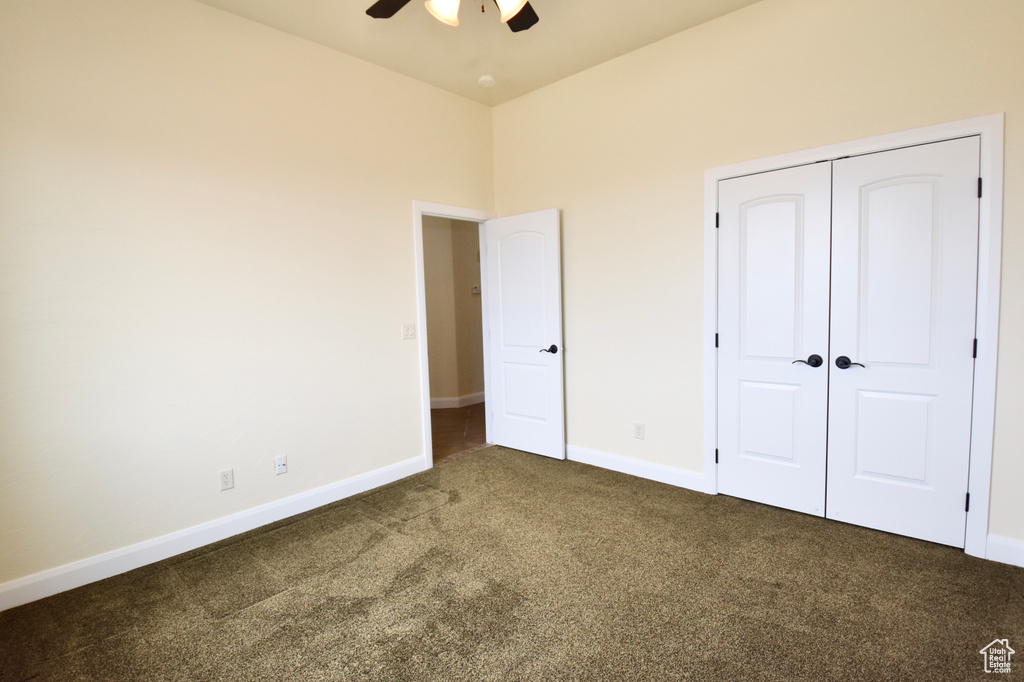 Unfurnished bedroom with a closet, dark colored carpet, and ceiling fan