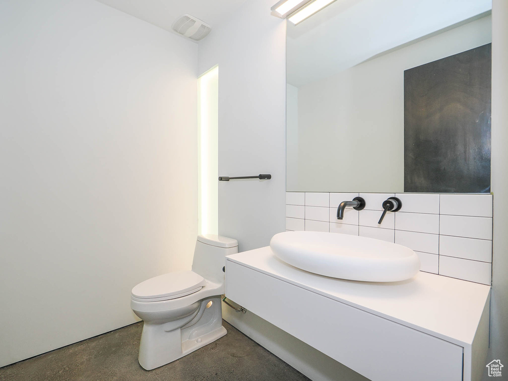 Bathroom featuring toilet, vanity, tile walls, concrete floors, and backsplash