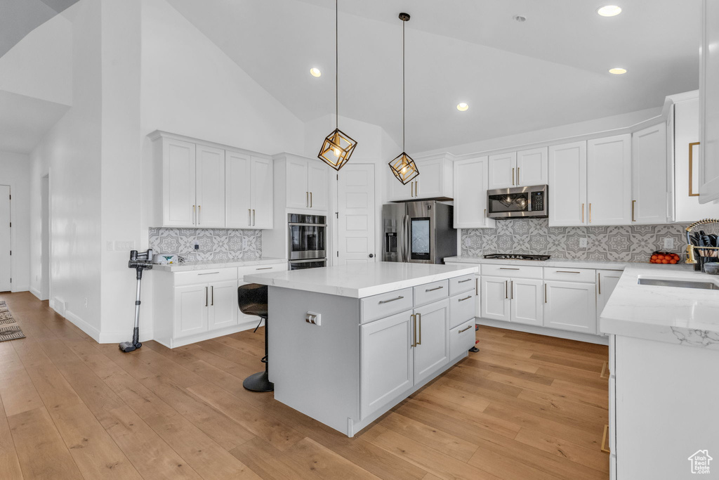 Kitchen featuring decorative light fixtures, high vaulted ceiling, light wood-type flooring, appliances with stainless steel finishes, and tasteful backsplash