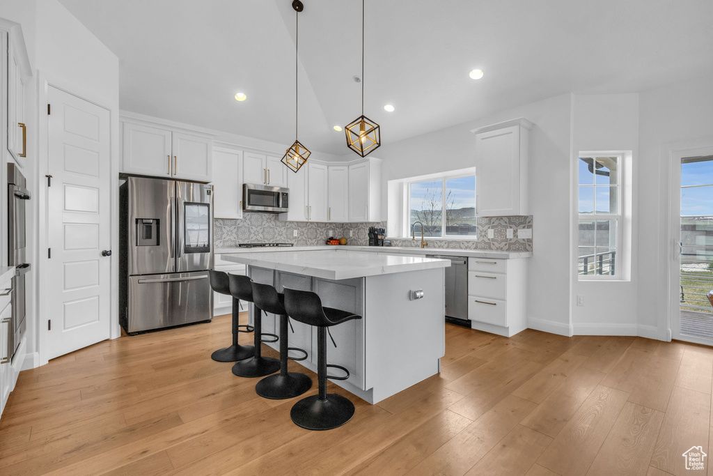 Kitchen with backsplash, light hardwood / wood-style flooring, stainless steel appliances, and decorative light fixtures