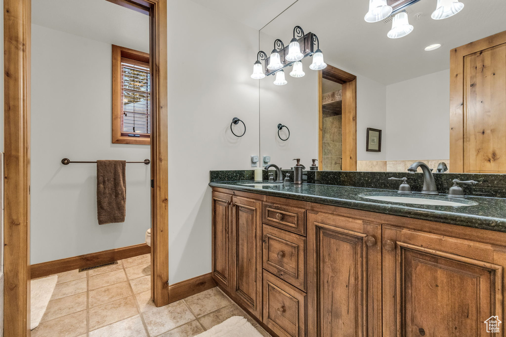 Bathroom with toilet, tile floors, double sink, and vanity with extensive cabinet space