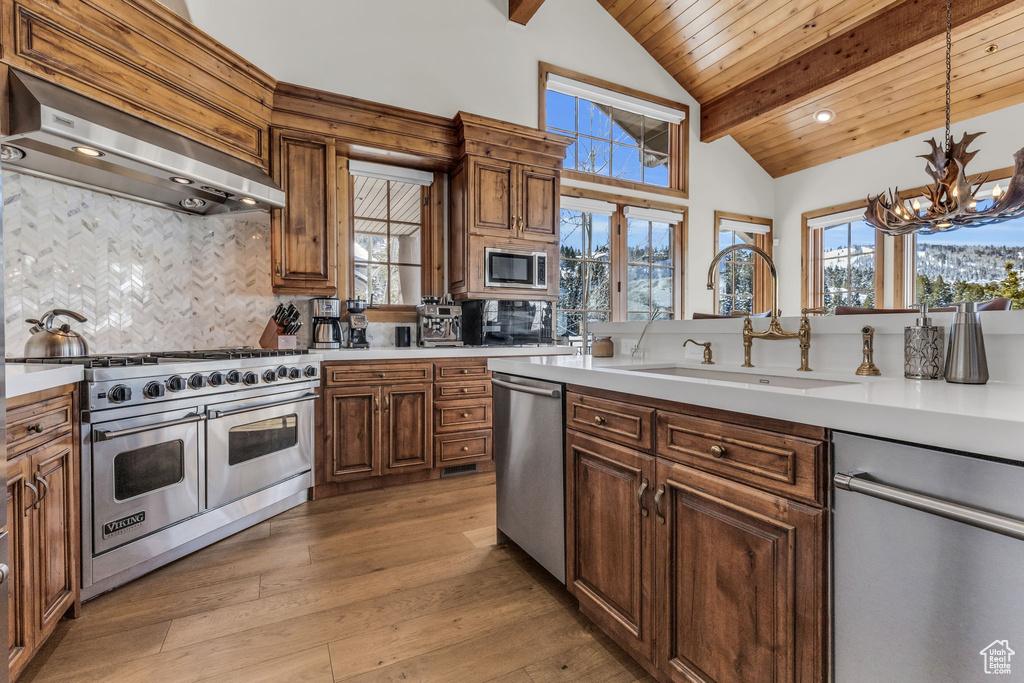 Kitchen featuring a chandelier, stainless steel appliances, wall chimney exhaust hood, decorative light fixtures, and light wood-type flooring