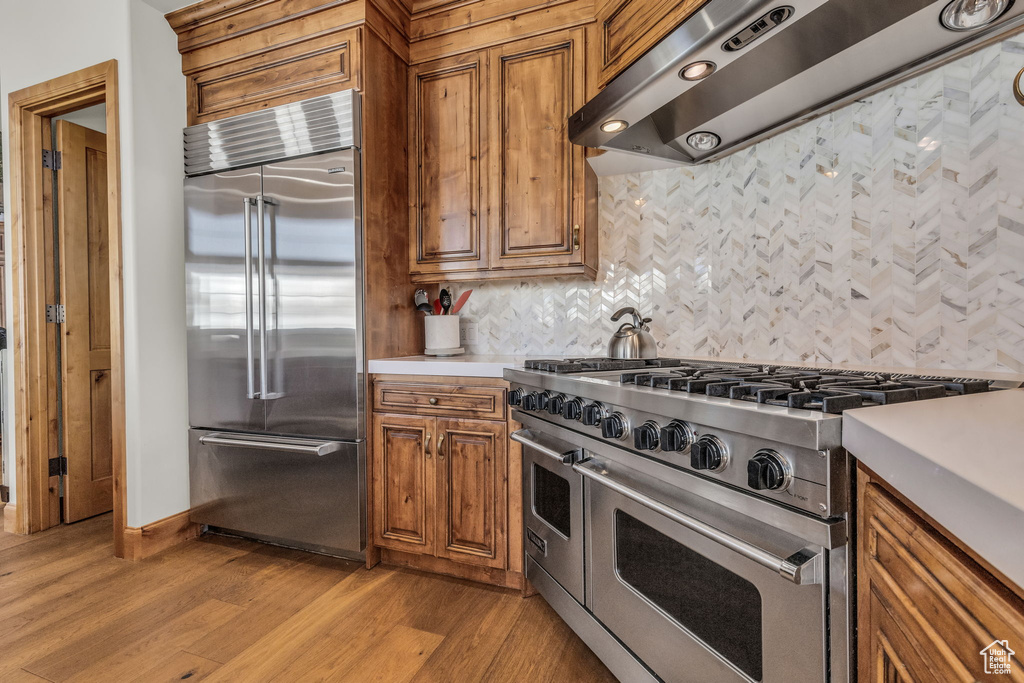Kitchen featuring premium appliances, tasteful backsplash, light hardwood / wood-style floors, and wall chimney range hood