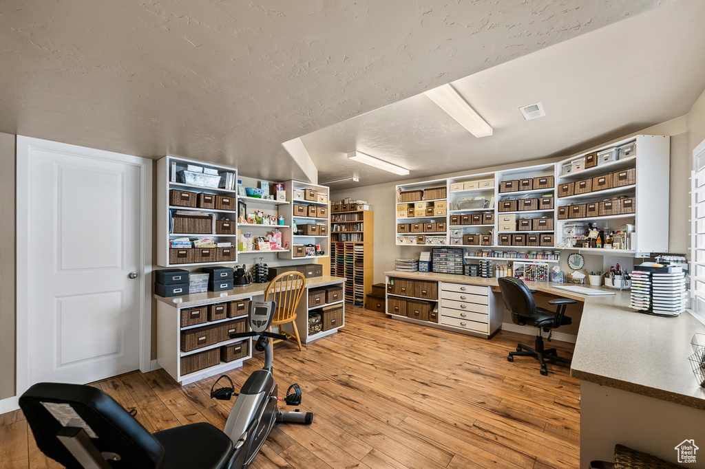 Office space featuring built in desk, light hardwood / wood-style floors, and a textured ceiling