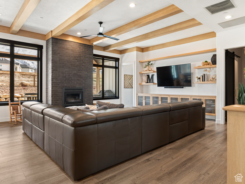 Living room with brick wall, a brick fireplace, ceiling fan, beamed ceiling, and light hardwood / wood-style flooring