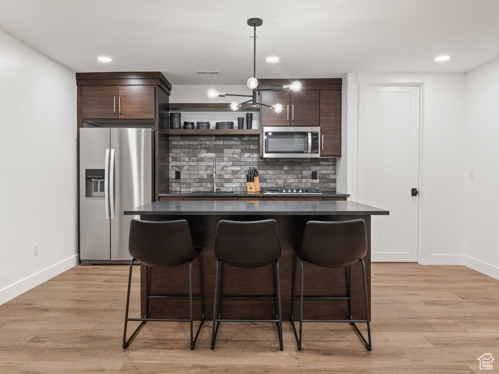 Kitchen with a notable chandelier, light wood-type flooring, dark brown cabinets, and appliances with stainless steel finishes
