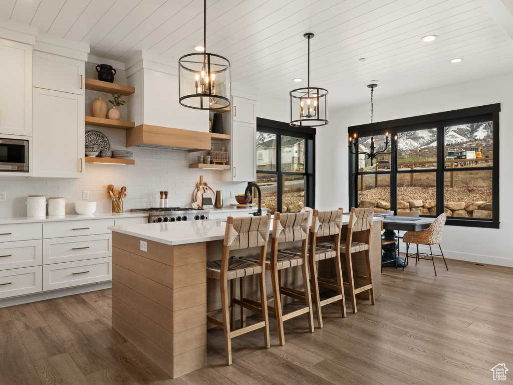 Kitchen with white cabinetry, backsplash, a center island with sink, hardwood / wood-style flooring, and pendant lighting