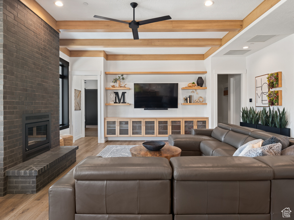 Living room with a fireplace, ceiling fan, light hardwood / wood-style flooring, and beam ceiling