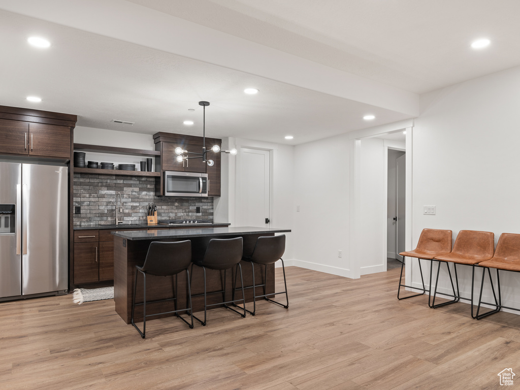 Kitchen with dark brown cabinets, light hardwood / wood-style flooring, a breakfast bar area, stainless steel appliances, and tasteful backsplash