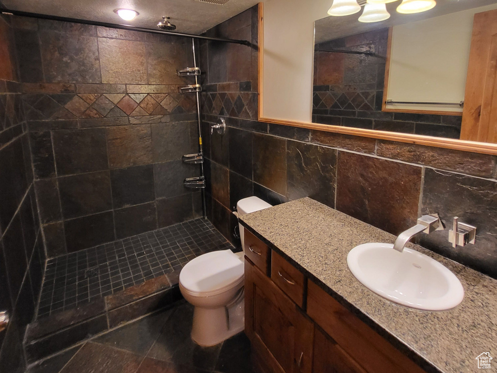 Bathroom with tile walls, toilet, tiled shower, backsplash, and vanity